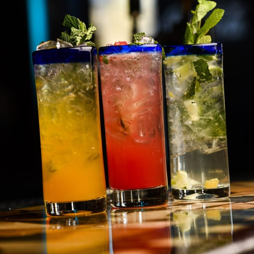 Three vibrant Blue Agave cocktails: yellow, red, and clear, garnished with mint and fruit.