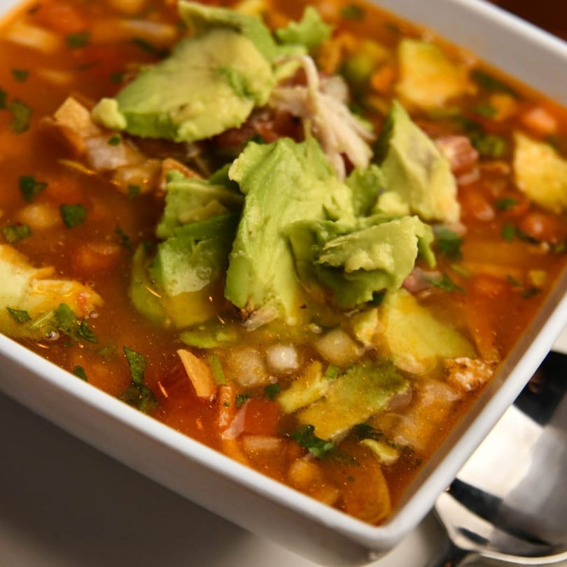 Close-up of Blue Agave's Mexican tortilla soup with avocado, chicken, and cilantro in a white bowl.
