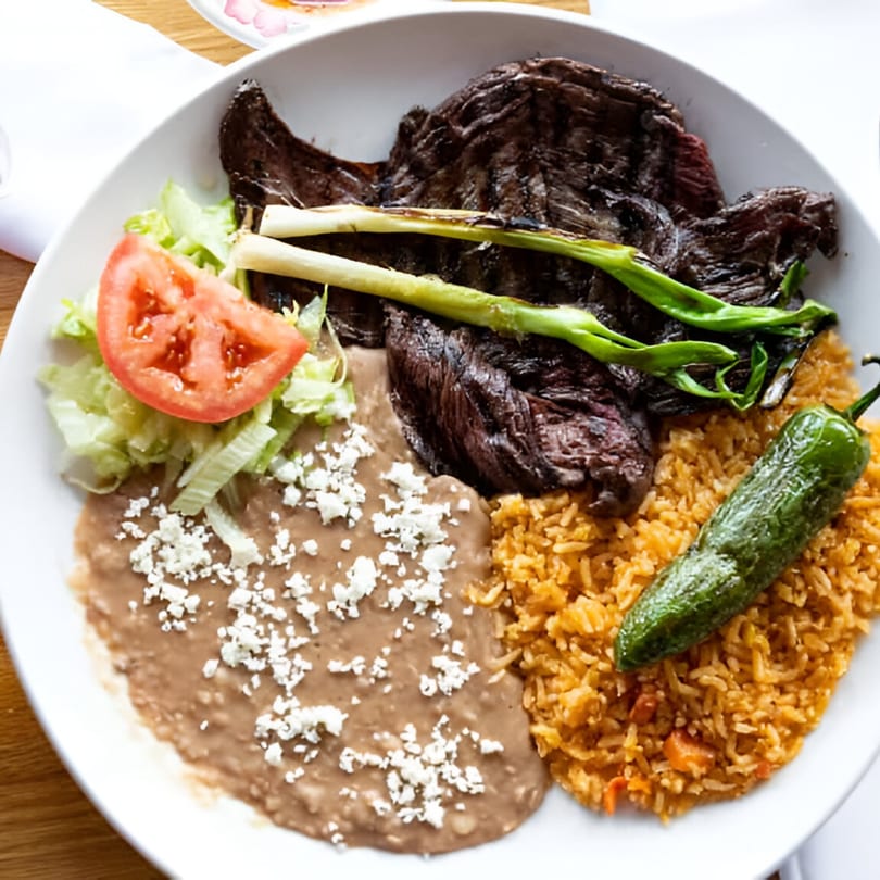 Mexican dish with grilled steak, refried beans, rice, a jalapeño, and a side salad.